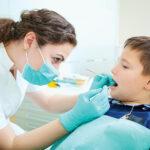 A female dentist performs a checkup on a child patient.