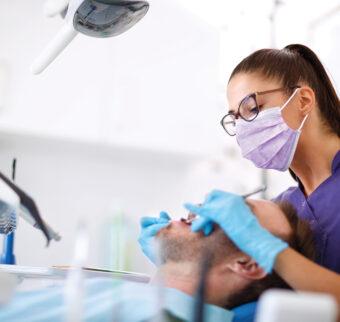 A female dentist performs a check up on a male patient.